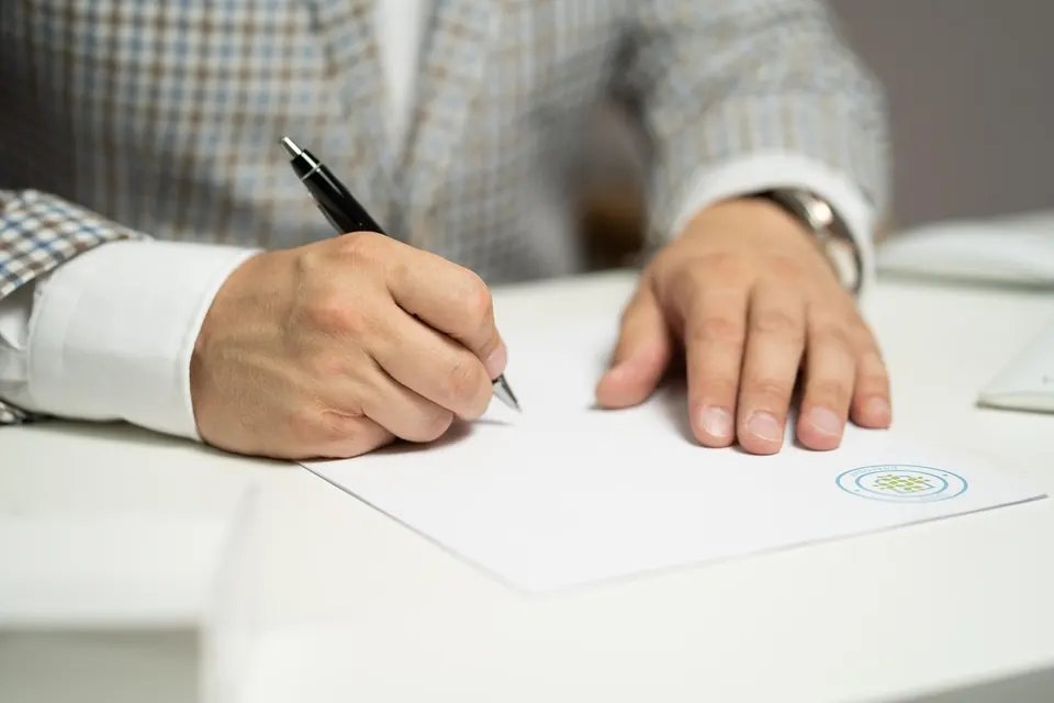 A person signing a document at a desk.