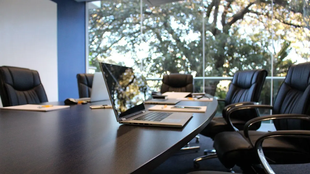An empty boardroom with a long dark table, leather chairs and daylight from a window.