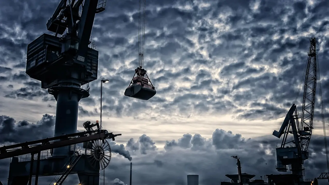 Container cranes at a shipping port silhouetted against a clouded sky.