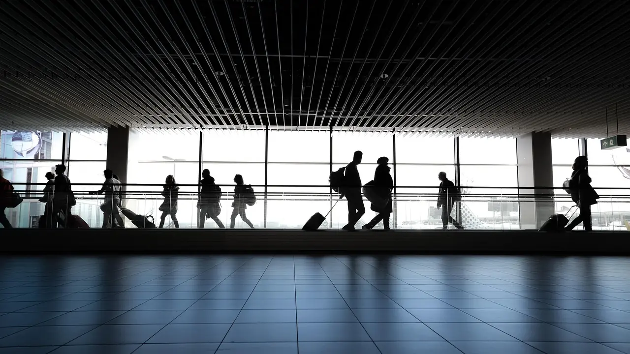 Travellers silhouetted against the glass wall of an airport terminal walkway.